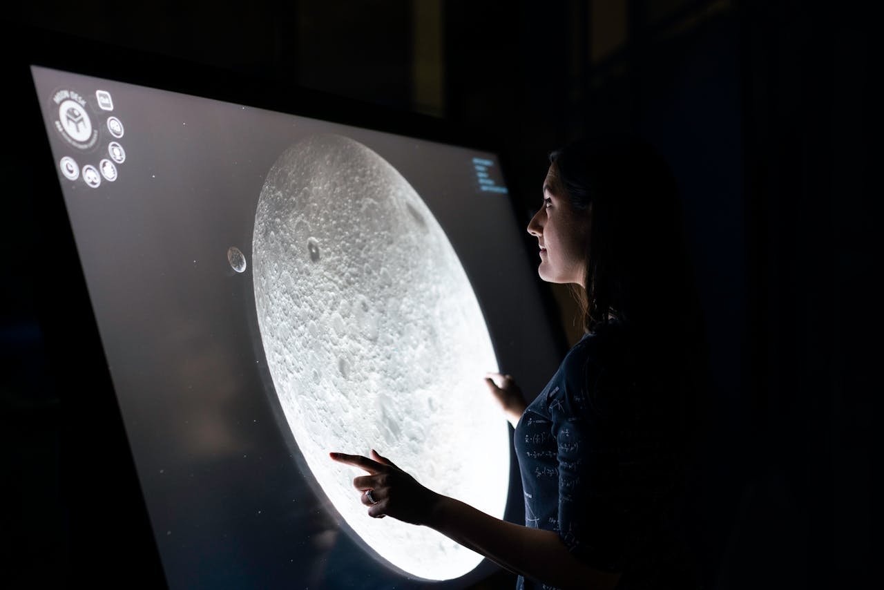 A woman interacts with a touchscreen showing the moon's surface, exploring lunar details.